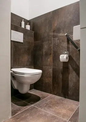 a bathroom with a toilet and brown tiles at Scheldeoever in Temse