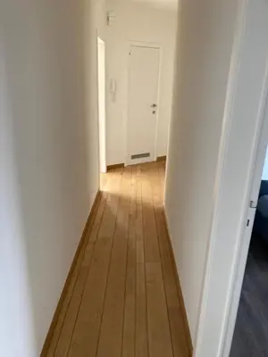 a hallway with a wooden floor and a white door at Lichtrijk mooi appartement met zicht op hof van Roosendael in Antwerp