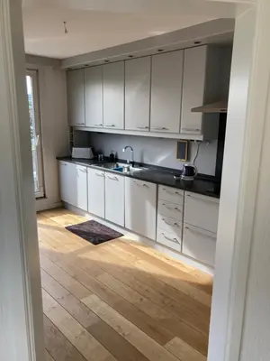 a kitchen with white cabinets and a wooden floor at Lichtrijk mooi appartement met zicht op hof van Roosendael in Antwerp