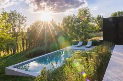 a pool in the middle of a garden with the sun shining at Wellness Suite B&B L'O Reine in Sint-Pieters-Leeuw