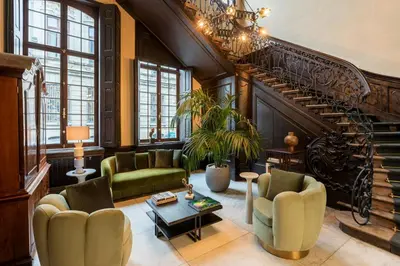 a living room with a staircase and green chairs at Sapphire House Antwerp, Autograph Collection in Antwerp