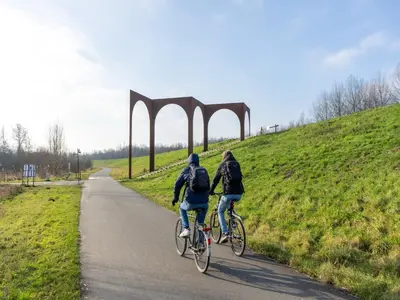 two people riding bikes down a road with a bridge at Apartment in Kruibeke Wissekerke Castle in Kruibeke