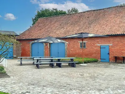 two picnic tables with umbrellas in front of a building at Alverwege in Merksplas