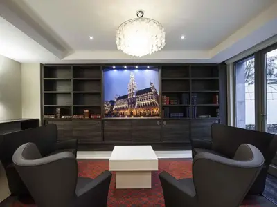 a living room with two chairs and a tv on a wall at Mercure Hotel Brussels Centre Midi in Brussels