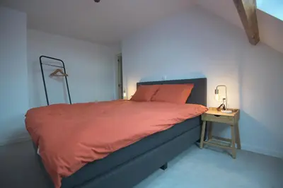 a bedroom with a bed with an orange comforter and a side table at Gastenkamers huYze K in Zottegem