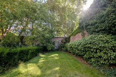 a garden with green grass and trees and a brick wall at La Calamande En Ville in Brussels