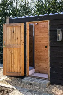 a wooden outhouse with a door and a porch at Comfort Tipi Marie, Tipi Bo Deluxe & tent Nicolaï - 'Glamping in stijl' in Lembeke