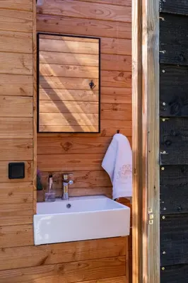 a bathroom with a white sink in a wooden wall at Comfort Tipi Marie, Tipi Bo Deluxe & tent Nicolaï - 'Glamping in stijl' in Lembeke