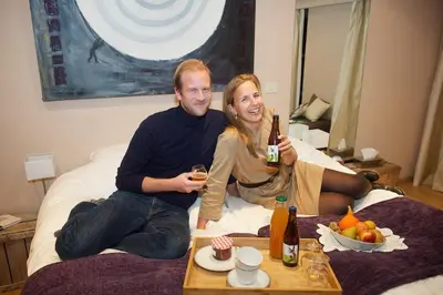 a man and woman sitting on a bed with drinks at B&B Vennehoeve in Vremde