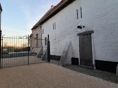 a white building with a wooden door next to a fence at Huis Potaerde, vakantiewoning op boerderij - luxe landhuis nabij Brussel in Merchtem