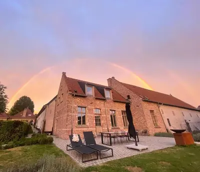 a rainbow over a brick building with chairs and a table at Huis Potaerde, vakantiewoning op boerderij - luxe landhuis nabij Brussel in Merchtem