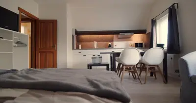 a bedroom with two white chairs and a kitchen at Berkies - autonome studio in Steenokkerzeel