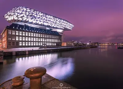 a large building with lights on the side of a body of water at On our way to Antwerp, first stop in Mortsel