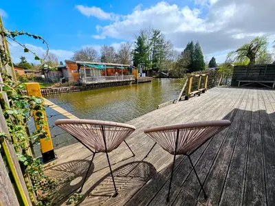 a couple of chairs sitting on a wooden deck next to a river at Le Canard - Rust aan het water in Geel
