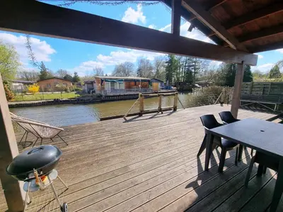 a wooden deck with a table and chairs and a river at Le Canard - Rust aan het water in Geel