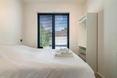 a white bedroom with a bed and a window at Design Studio Gent nabij station, musea &centrum in Ghent