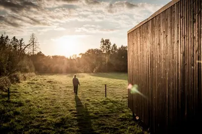 a man walking in a field with the sun setting at Kalmdown Cabin - Antwerp in Wuustwezel