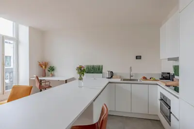 a white kitchen with a white counter and chairs at Center Royal Residence in Brussels