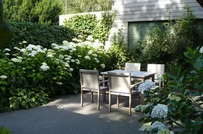 a table and chairs in a garden with white flowers at Holiday Home and Office Domisi'l in Wachtebeke