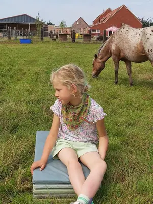 a little girl sitting on a book with a horse at Hoeve Megusta in Vlimmeren