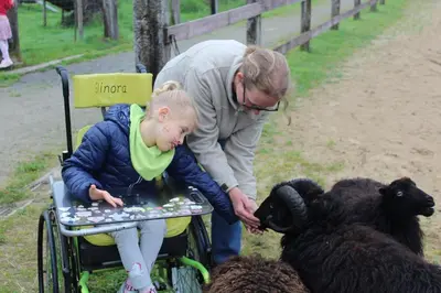 a woman and a girl in a wheelchair petting a black sheep at Hoeve Megusta in Vlimmeren