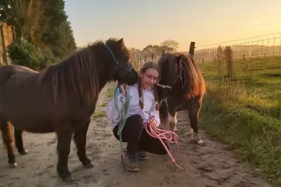 a woman kneeling down next to two horses on a dirt road at Hoeve Megusta in Vlimmeren