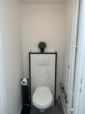 a white bathroom with a toilet and a plant on the wall at L Escapade Urbaine in Brussels