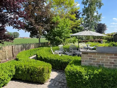a garden with a table and chairs and an umbrella at Sfeervol familielandhuis in de groene Kempen in Baarle-Hertog