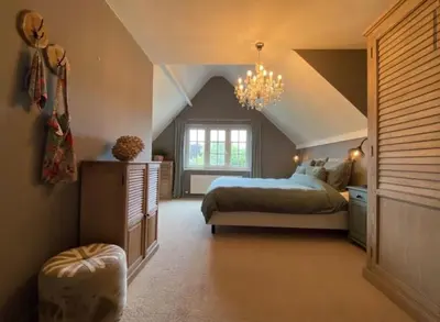 a attic bedroom with a bed and a chandelier at Sfeervol familielandhuis in de groene Kempen in Baarle-Hertog