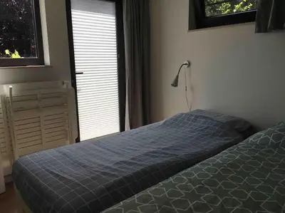 a bedroom with a bed with a blue blanket and a window at 'het T-huisje' volledig ingerichte studio in Leuven