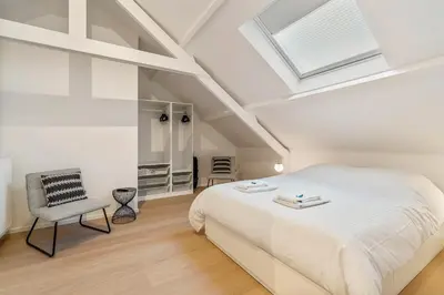 a white bedroom with a bed and a chair at Mooie vernieuwde Duplex in hartje Gent , Patershol in Ghent