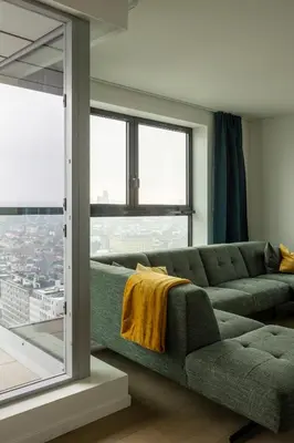 a living room with a green couch and a large window at UNIEK appartement - mooiste en hoogste uitzicht op Antwerpen! - incl gratis parking in Antwerp