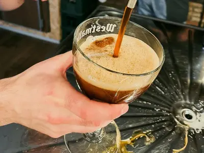 a person holding a glass with a drink at De Kasteelhoeve in Westmalle