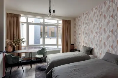 a bedroom with two beds and a table and a window at Hey - Aparthotel Brussels in Brussels