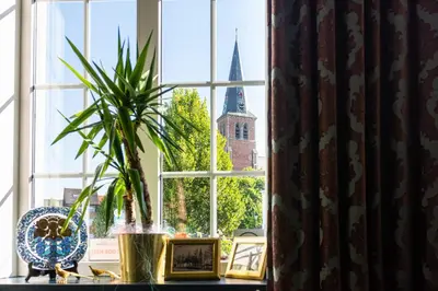 a window with a potted plant and a church at Boutique hotel Sies in Watervliet