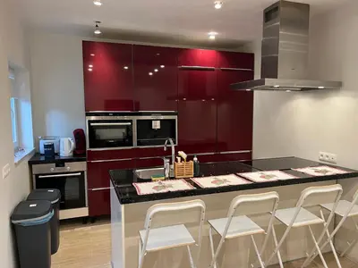 a kitchen with red cabinets and a counter with white stools at Les Cerisettes in Wavre